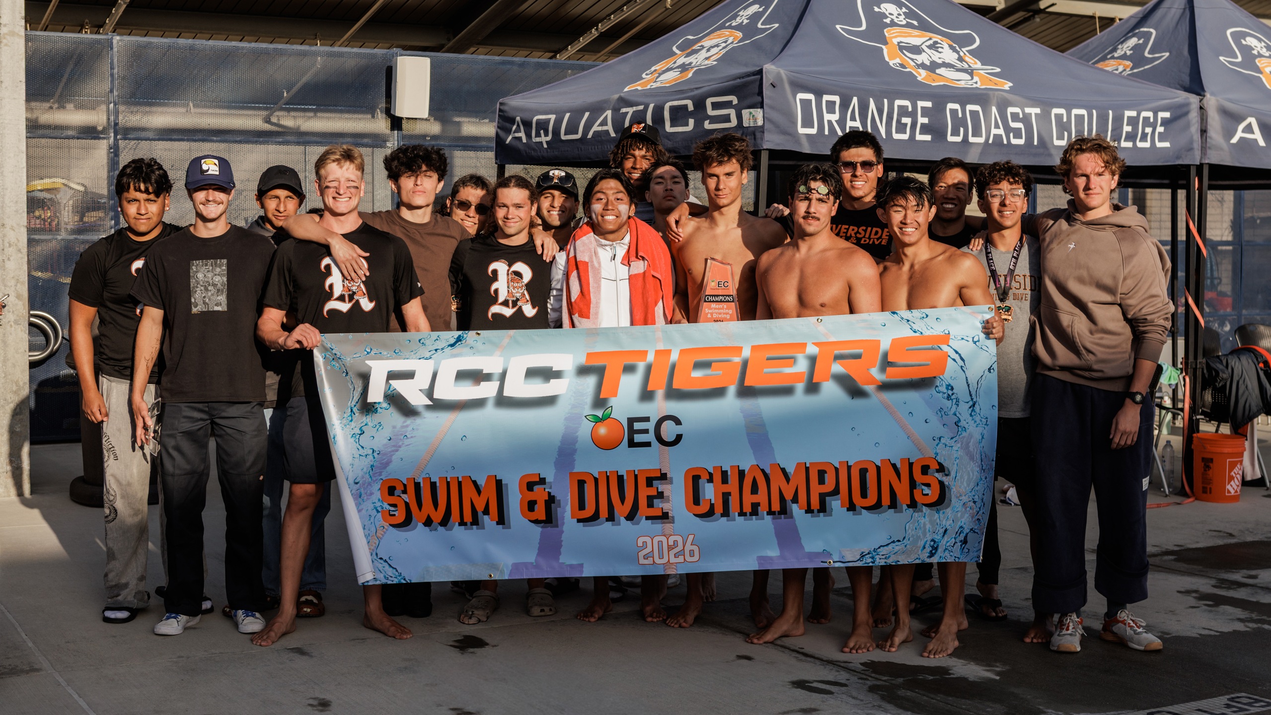 RCC men's swim and dive team poses with a banner that says "RCC Tigers OEC Swim & Dive Champions"