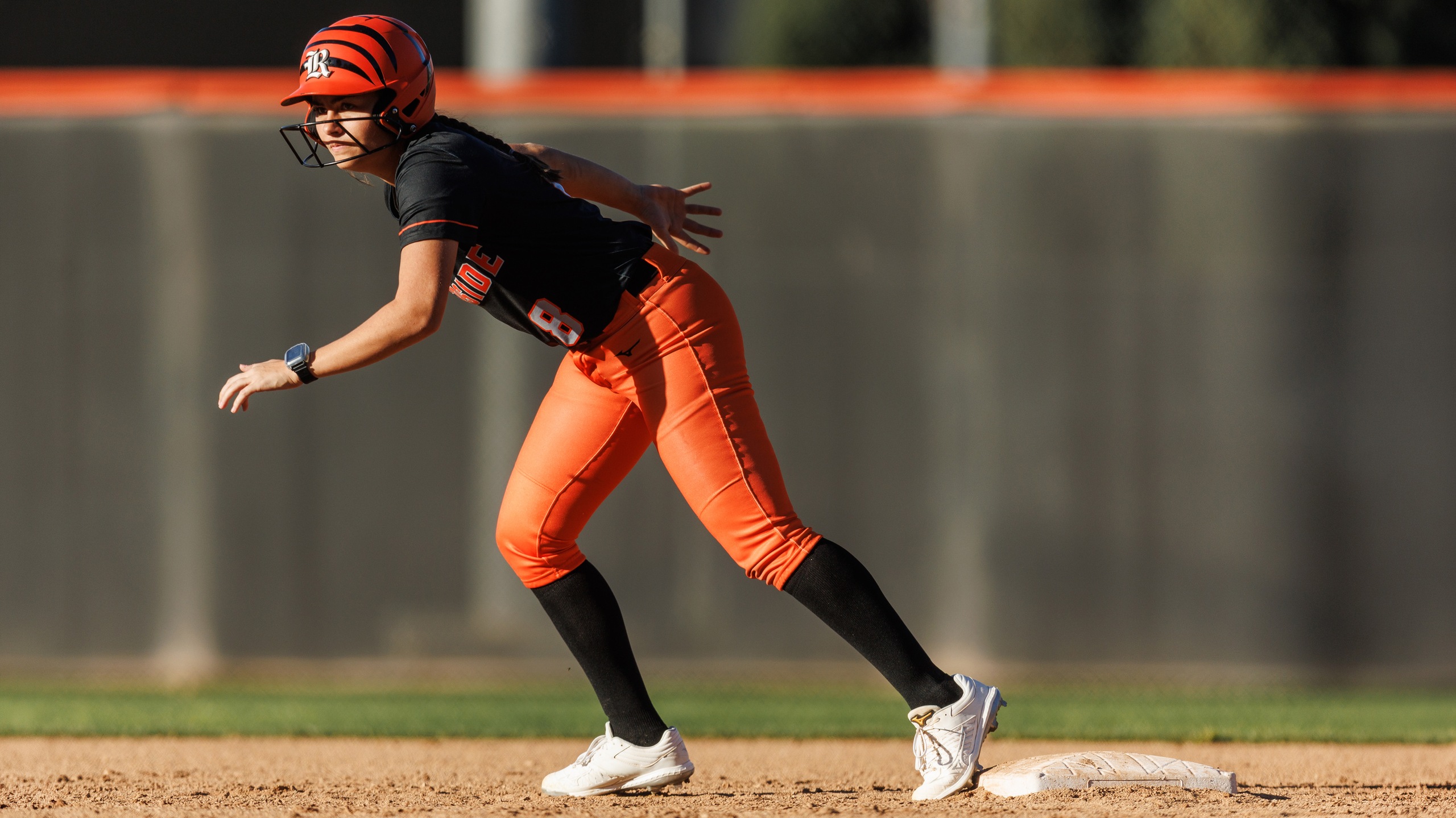 Softball player in black and orange uniform gets ready to run the bases