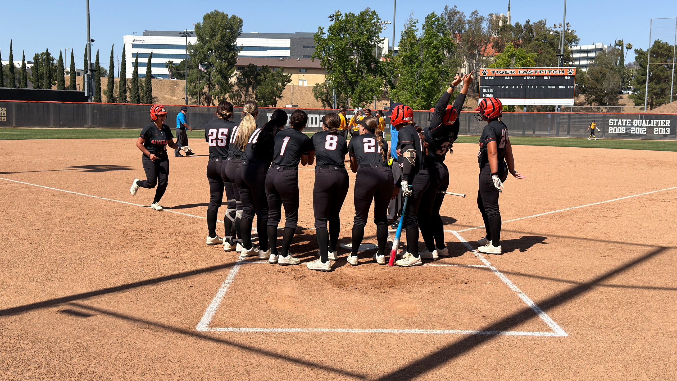 A group of softball players huddle together at the plate to celebrate a home run.