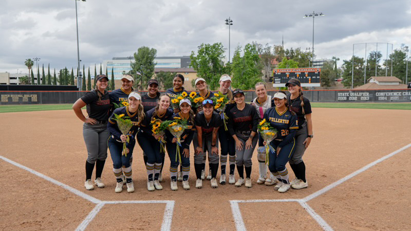 Group of softball players in dark uniforms pose together, smiling