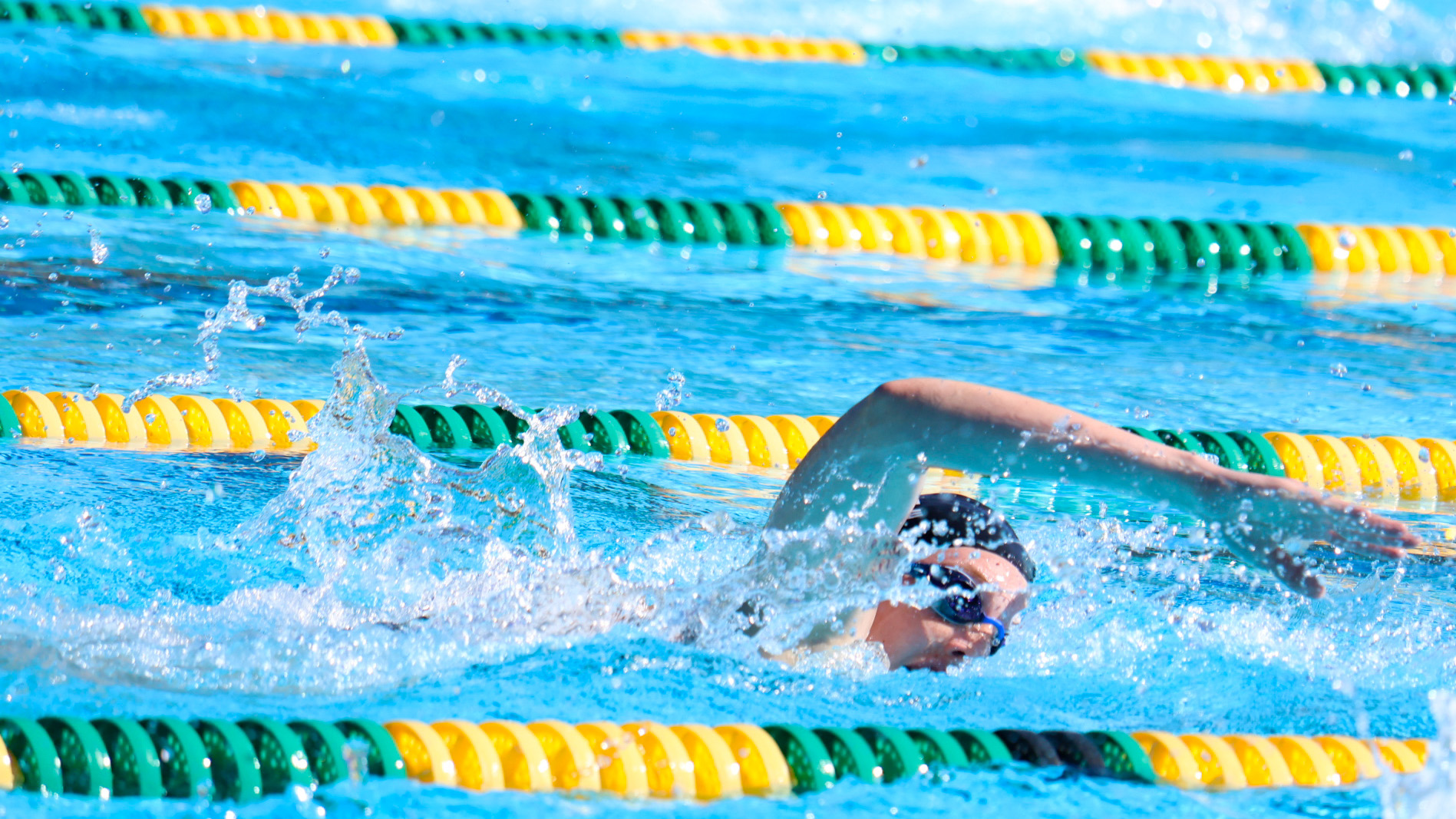 A female swimmer with a black cap and goggles swims through the water