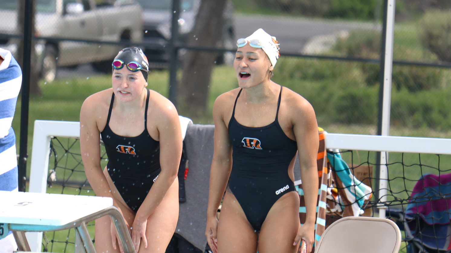 Two female swimmers cheer on their team at the pool